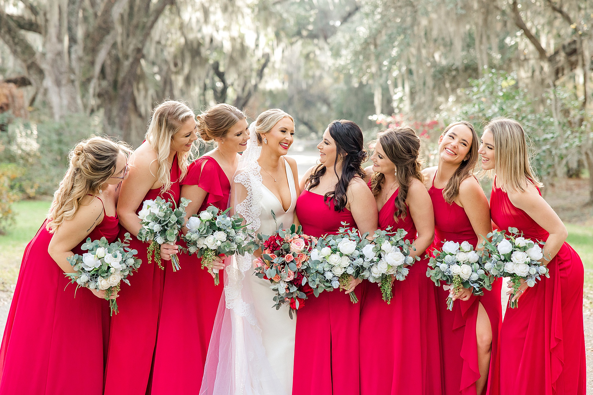 bridesmaids in red dresses and white bouquets stand around bride