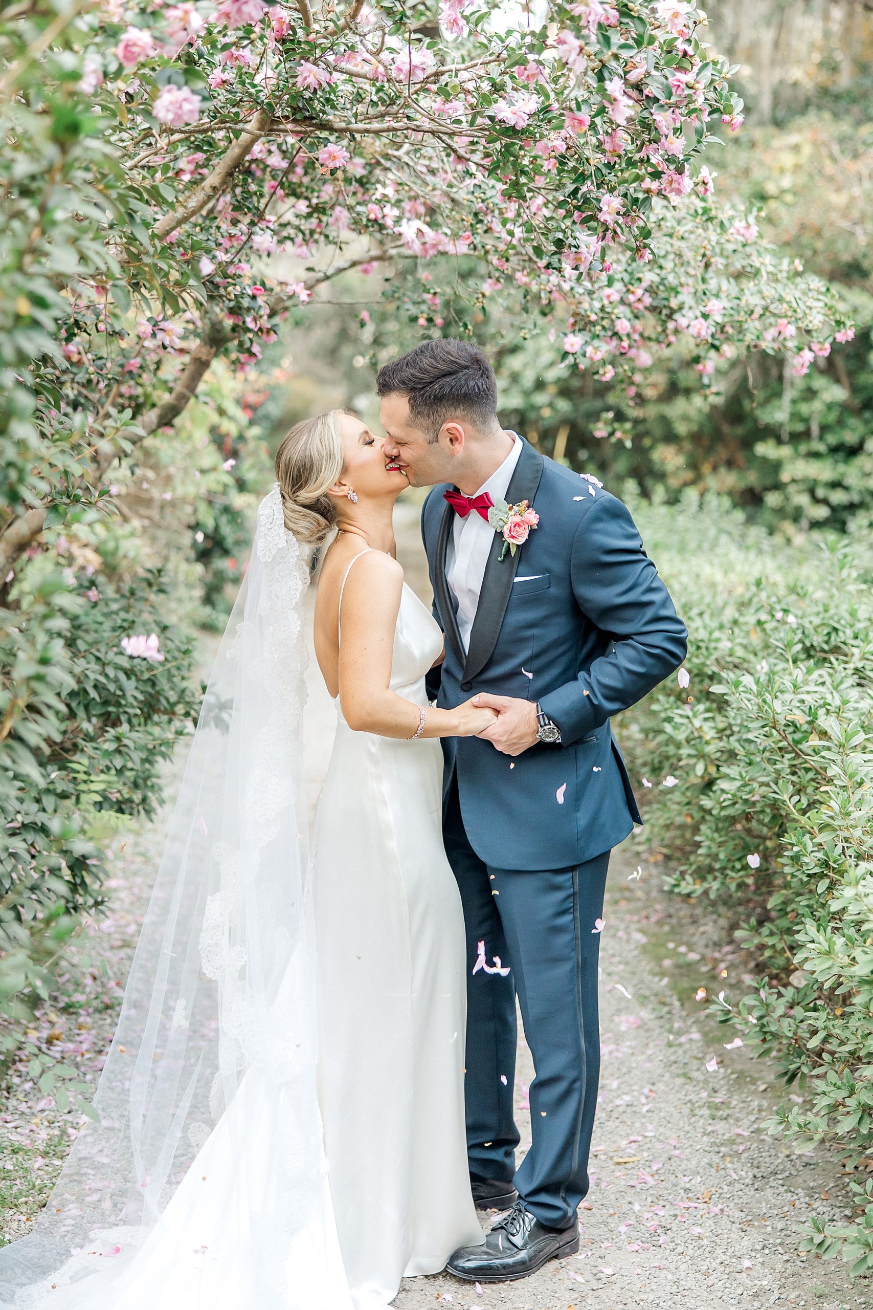 bride and groom kiss under tree with blooming flowers