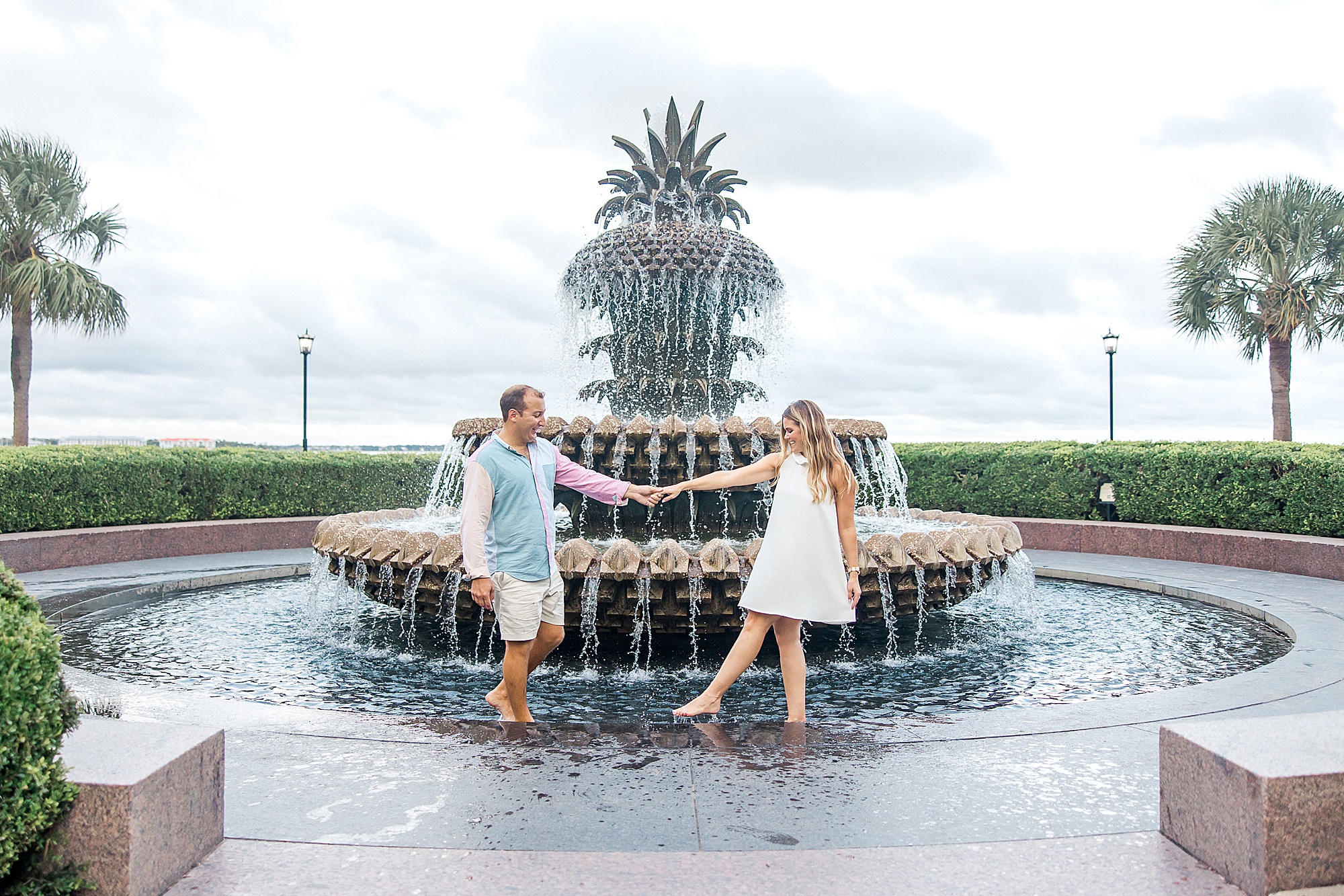 man splashes with his fiance in front of the pineapple fountain in Charleston SC