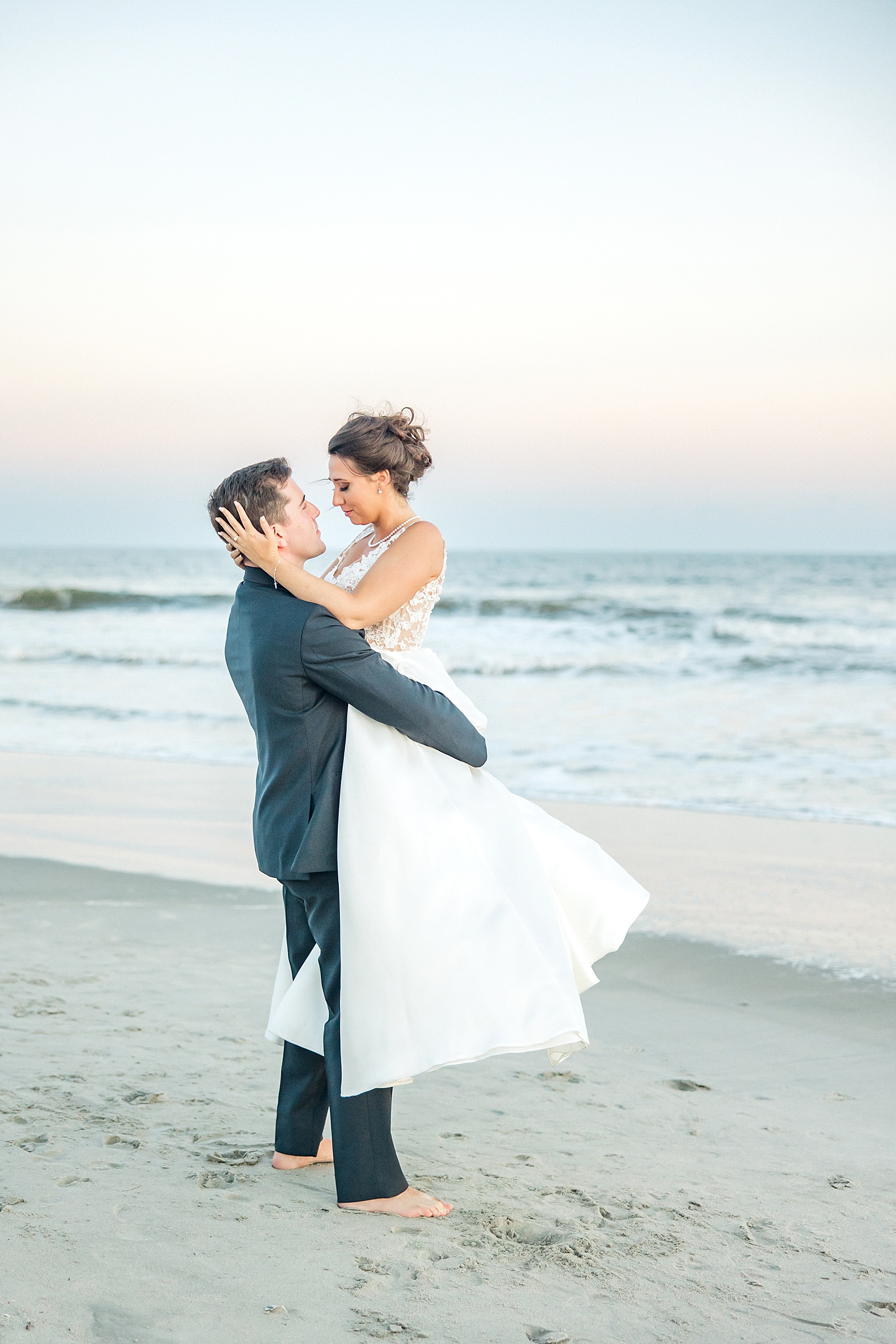 husband lifts his bride up on the beach