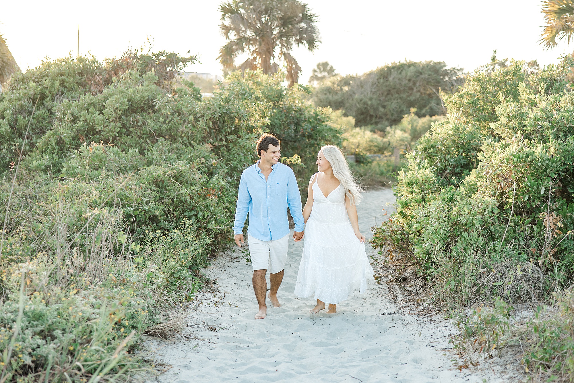 couple walk holding hands down sandy path at Folly Beach
