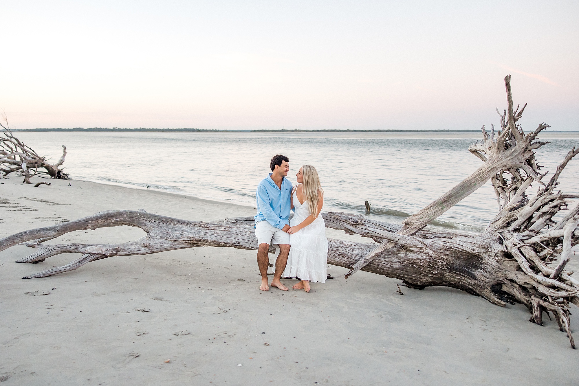 couple sit on driftwood during engagement portraits