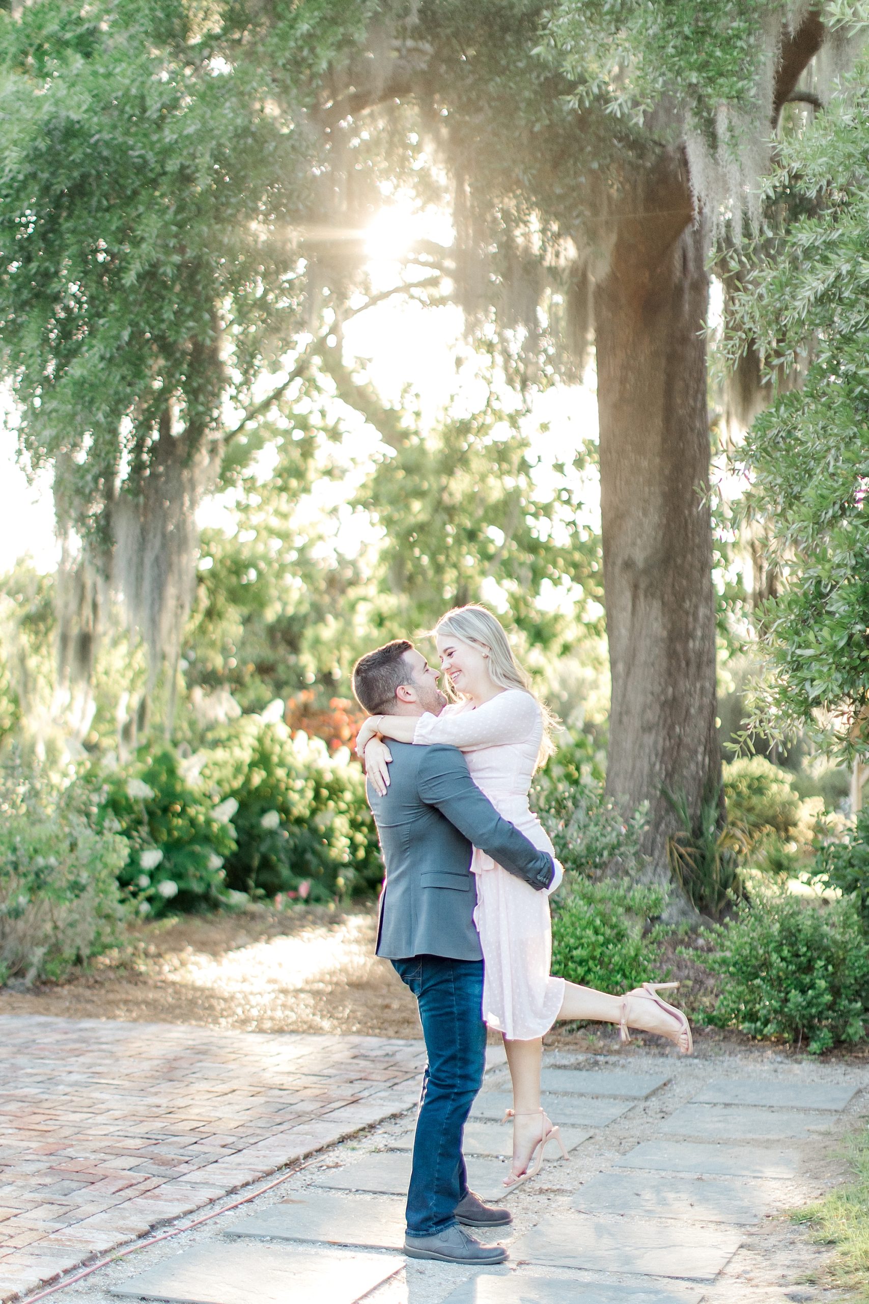 man lifts fiance up as sunshine gleams through the trees