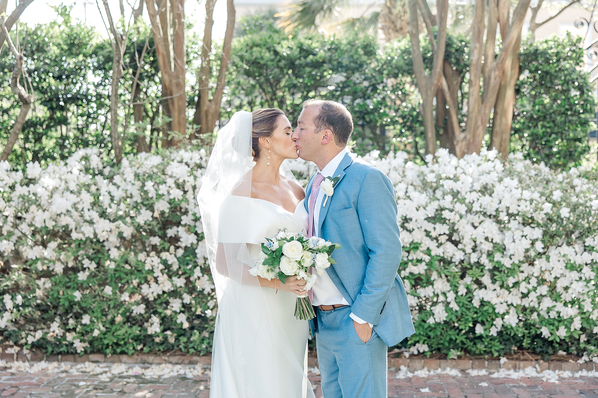 couple kiss in front of blooming bushes with white flowers