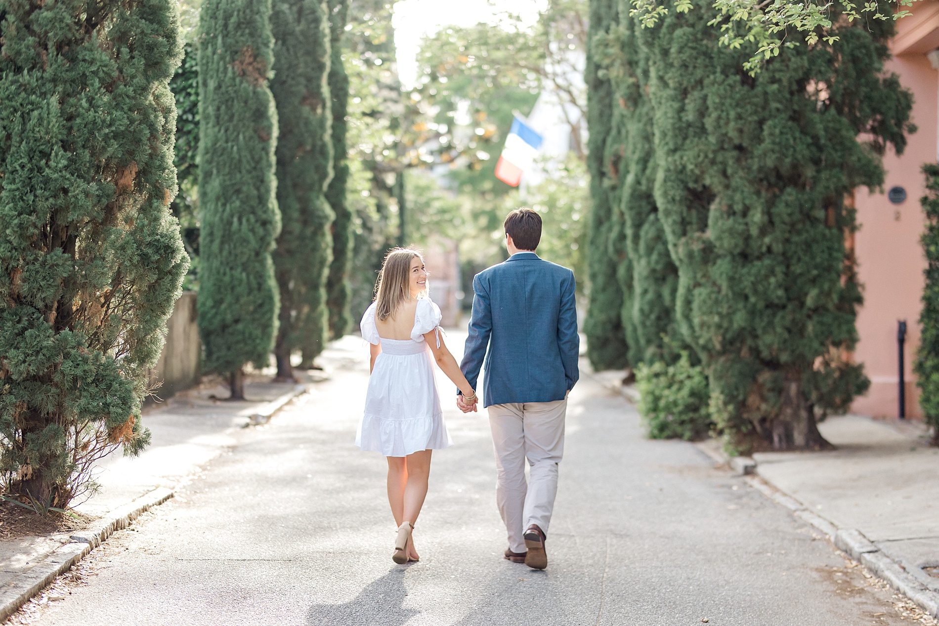 couple hold hands and walk along tree lined path