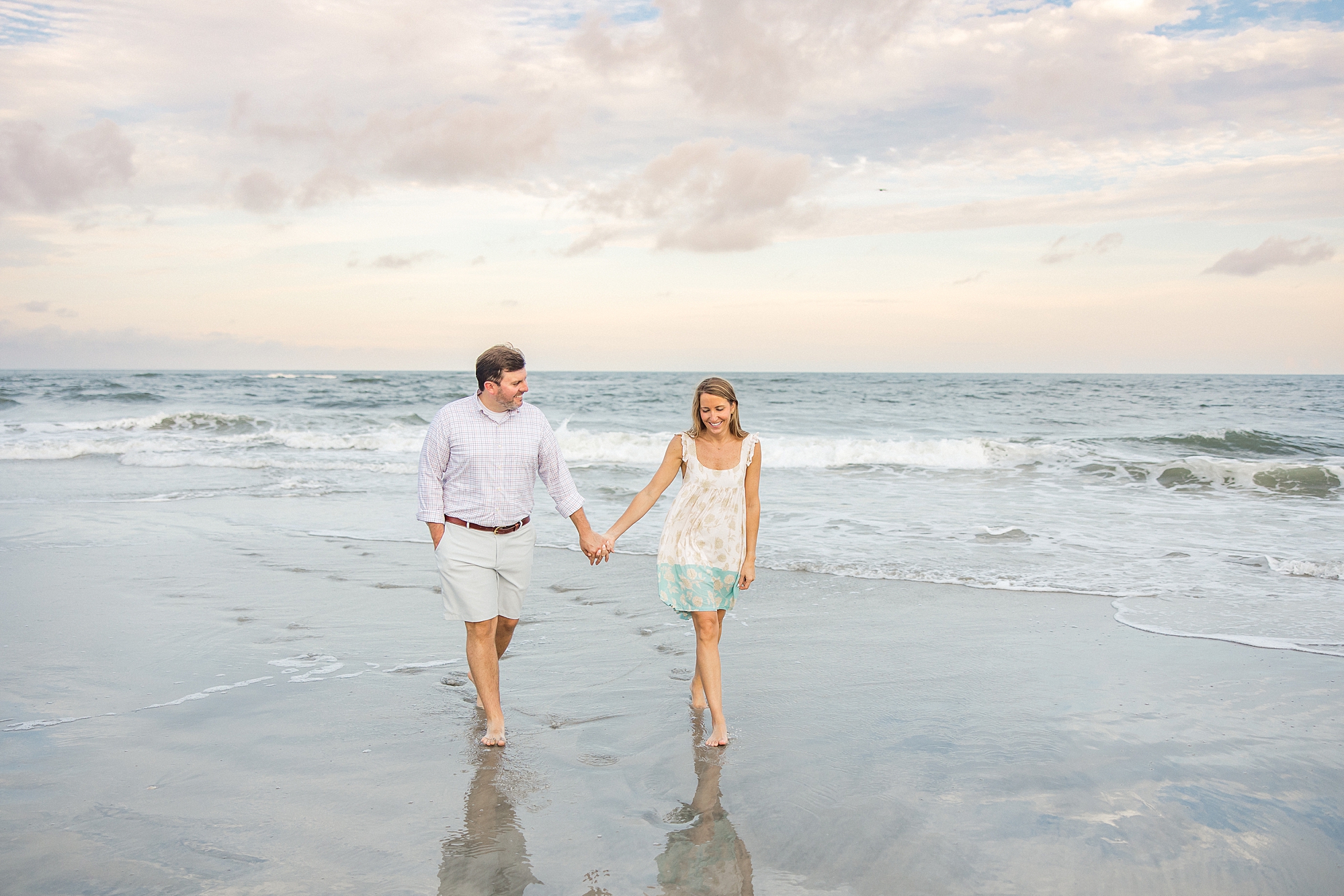 engaged couple walk on beach holding hands