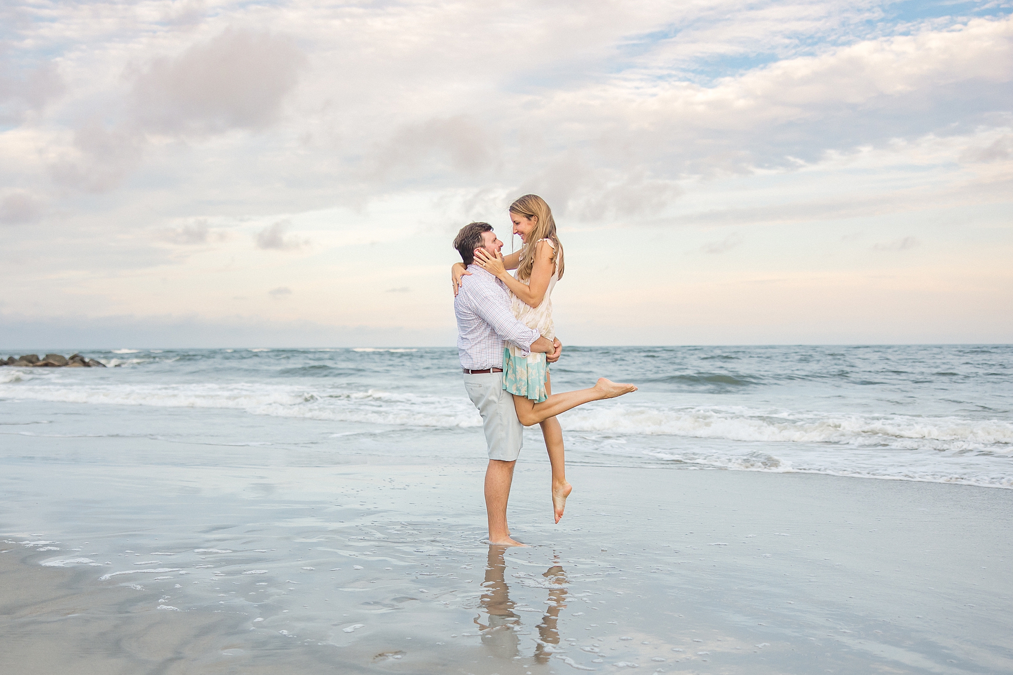 man lifts his fiance up on the beach
