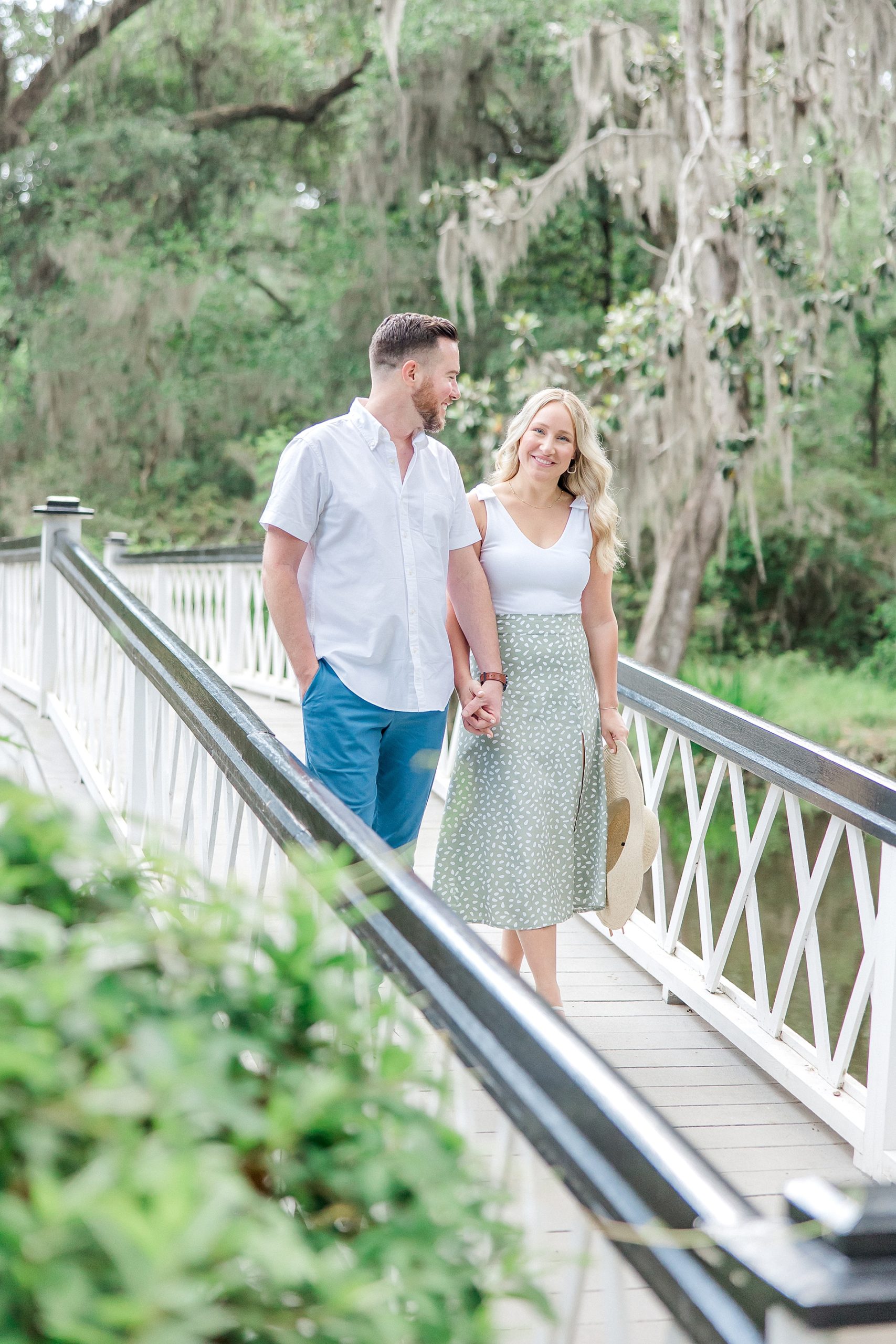 engaged couple walk across white bridge at Magnolia Plantation and Gardens