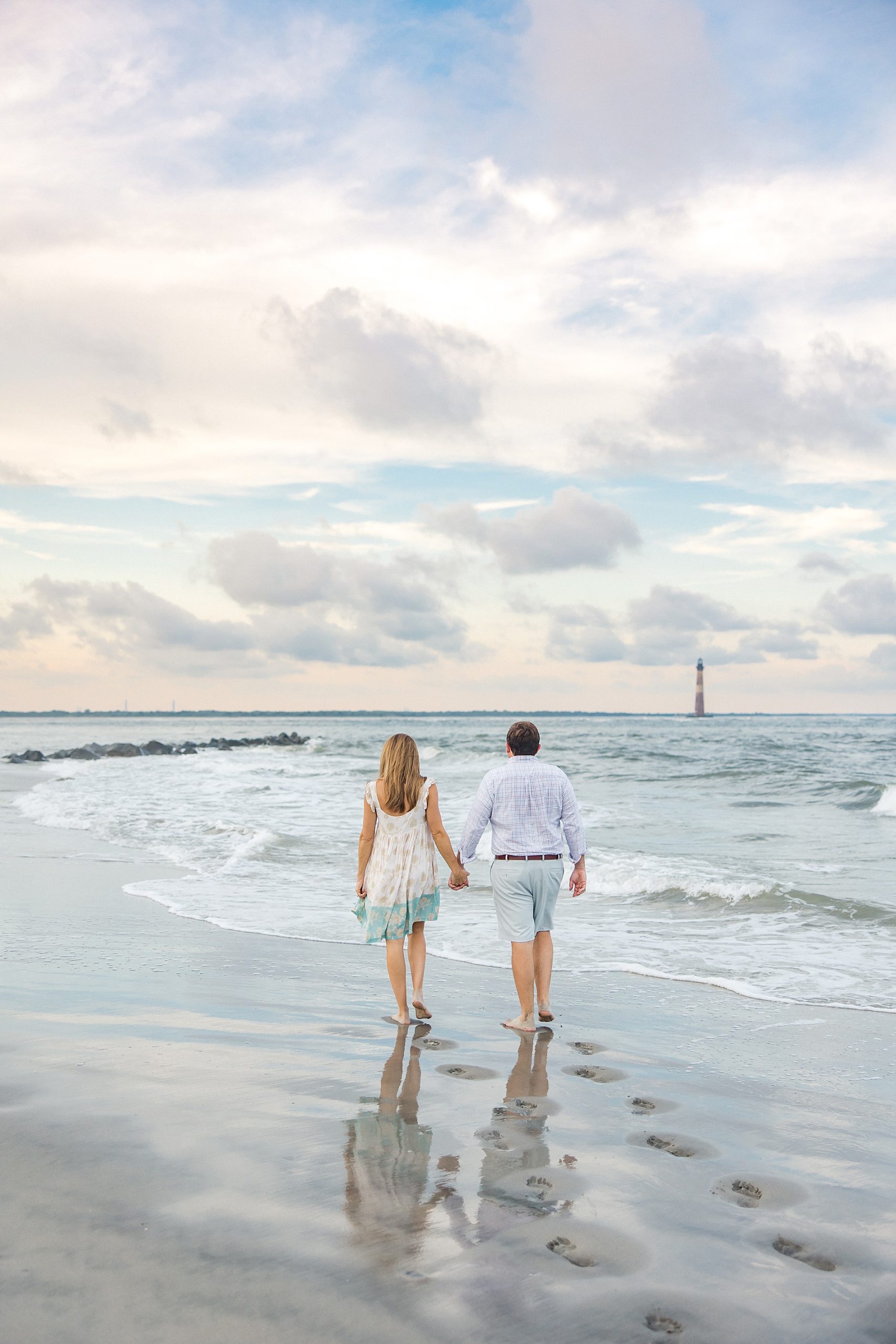 couple walk along the shoreline towards lighthouse