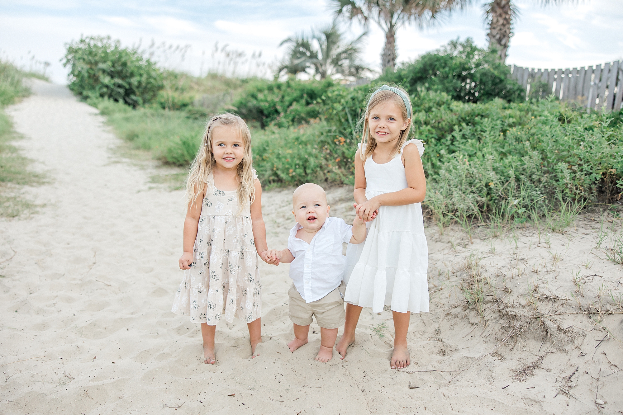 three siblings hold hands on the beach