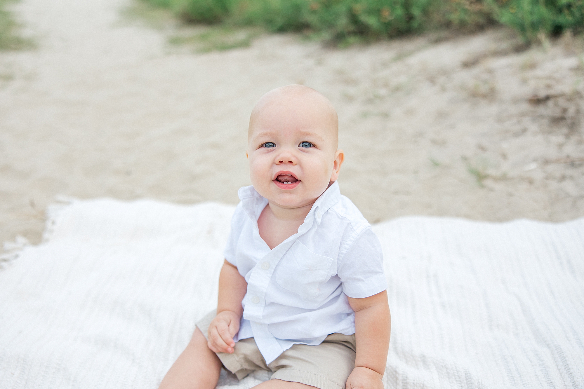 baby boy sits on white blanket on the beach