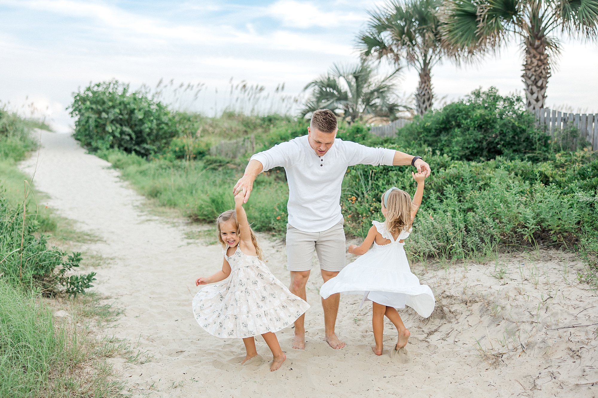 dad twirls his two daughters around at the beach