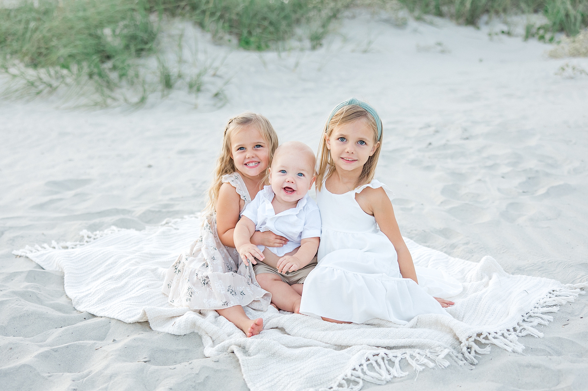 two older sisters sit with their baby brother on the beach