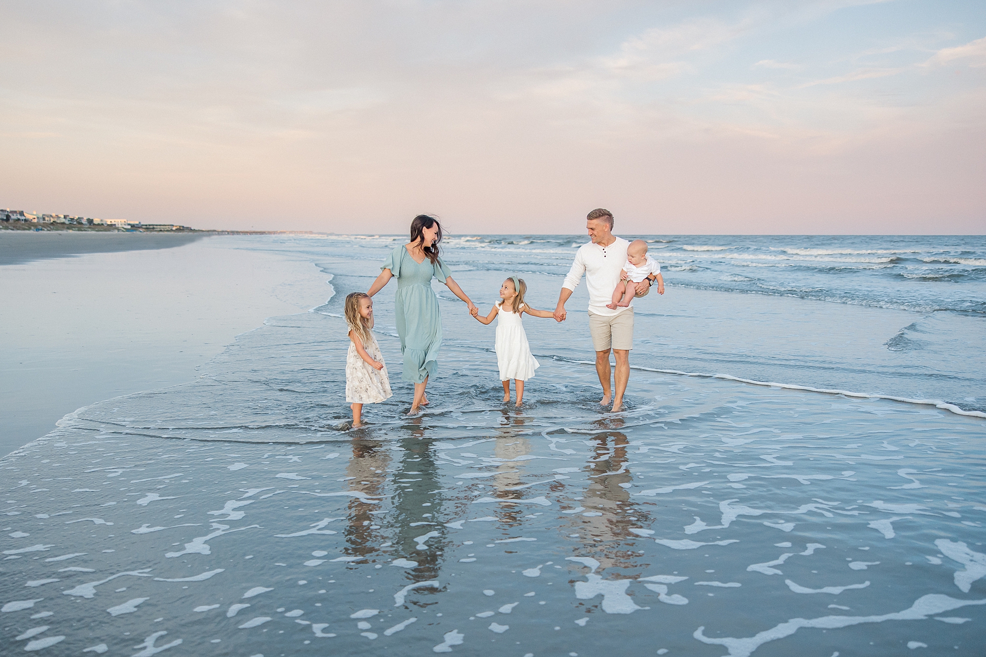family of five walks along the beach in the water