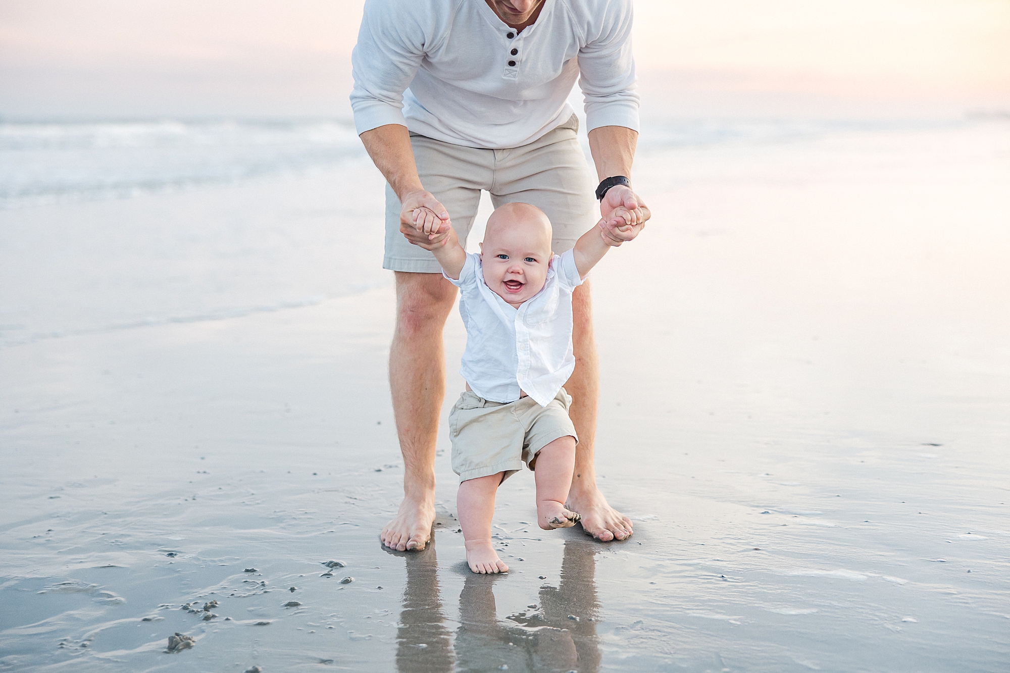 dad helps infant son walk along the beach