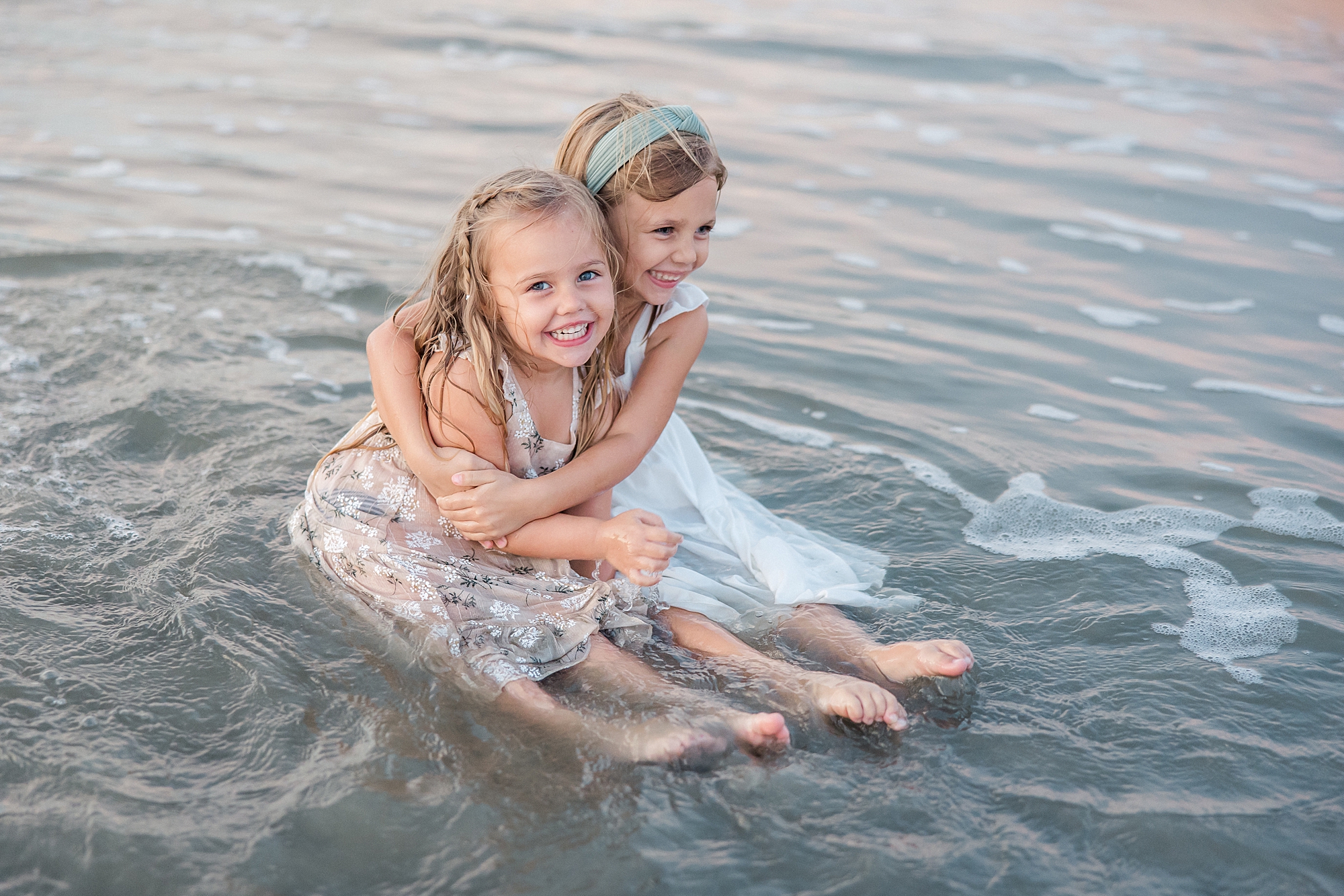 sisters hug as they sit in the shallow water