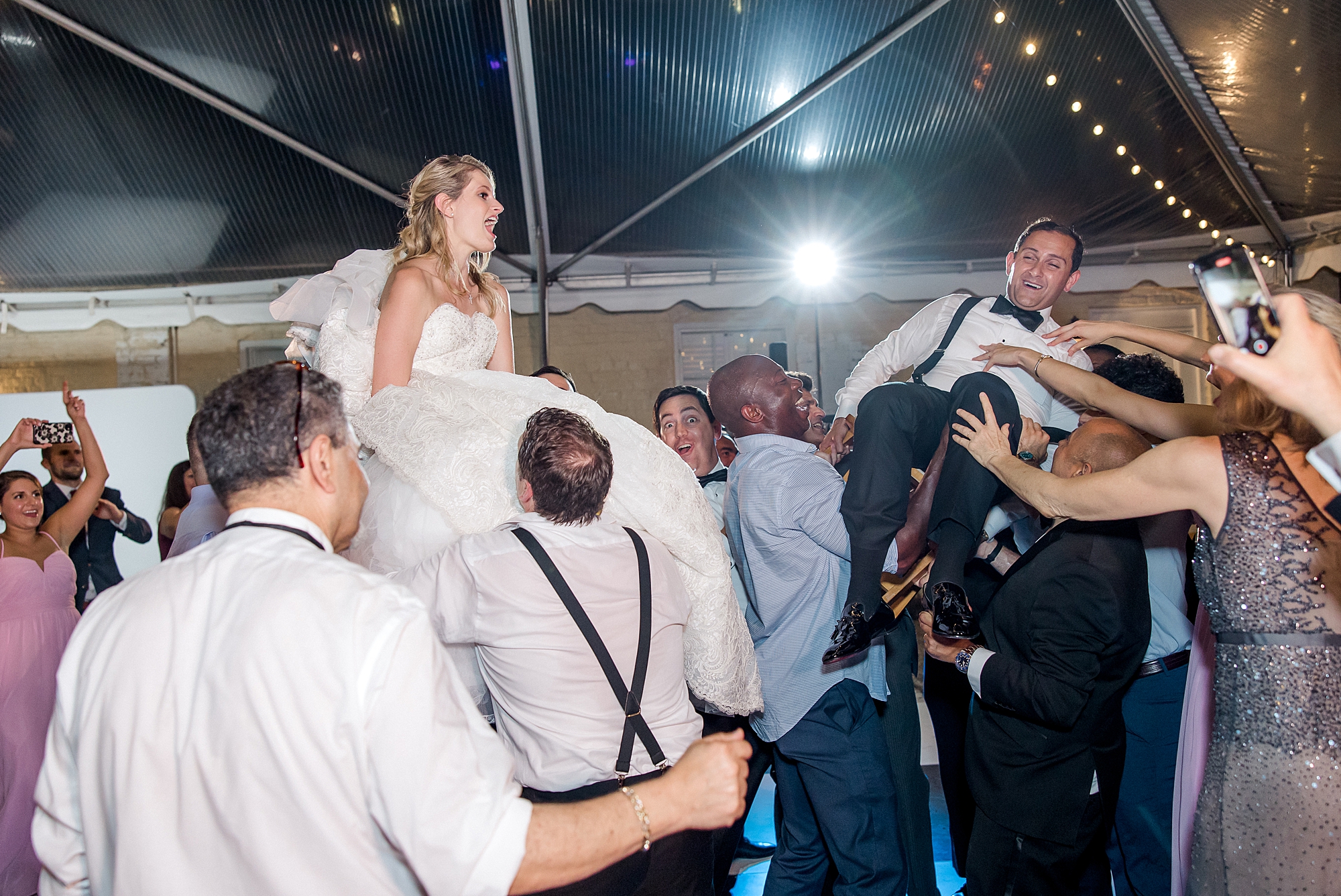 wedding guests lift bride in chair at wedding reception