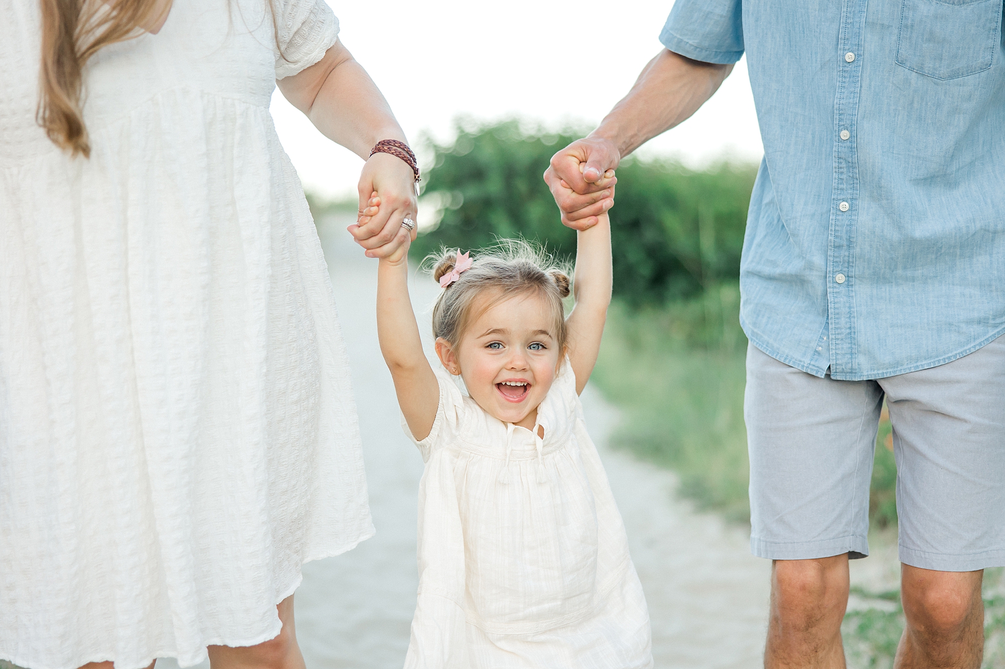 parents hold little girl's hands during family session at the beach