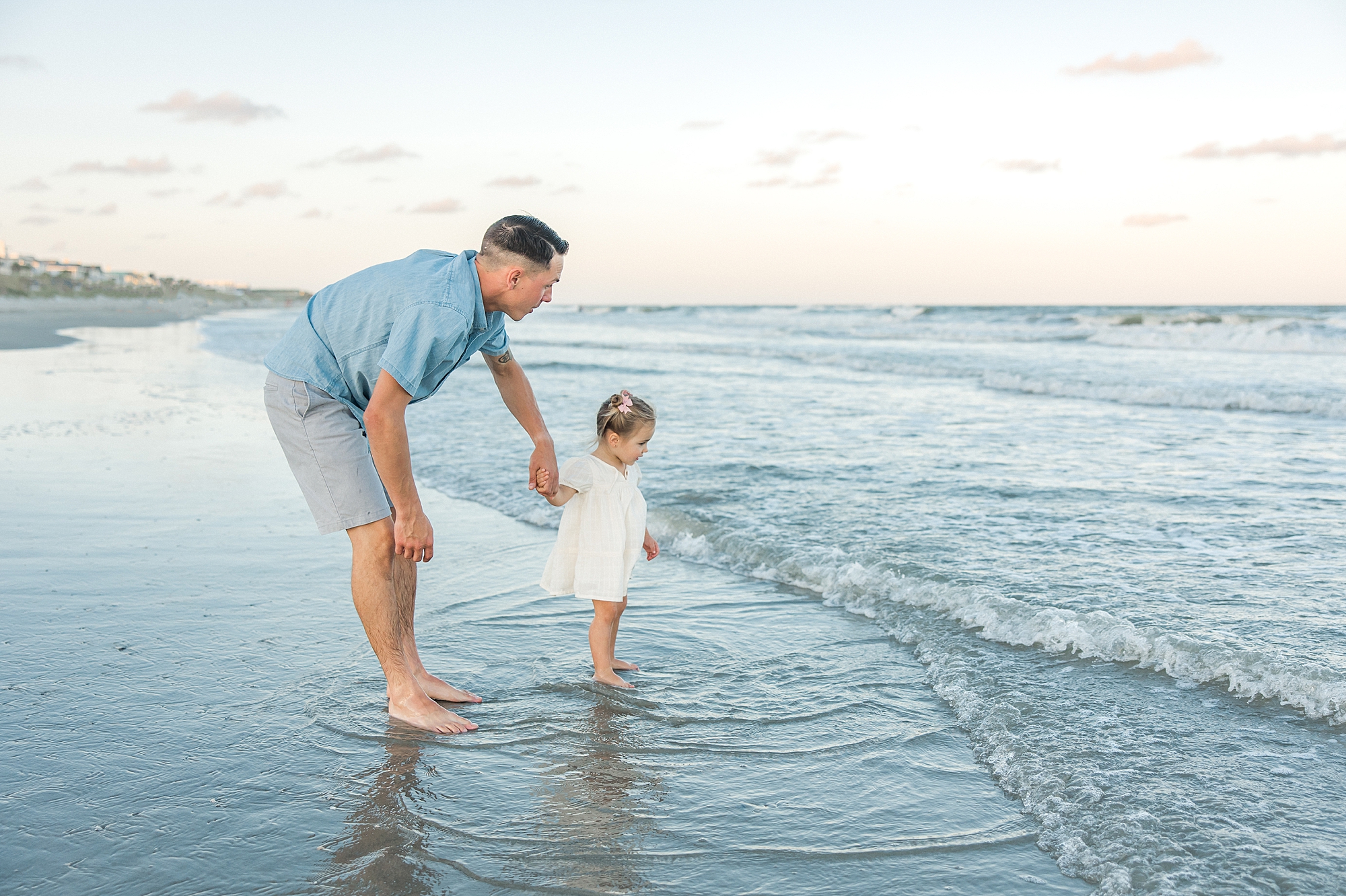 dad hold's daughter's hand by ocean