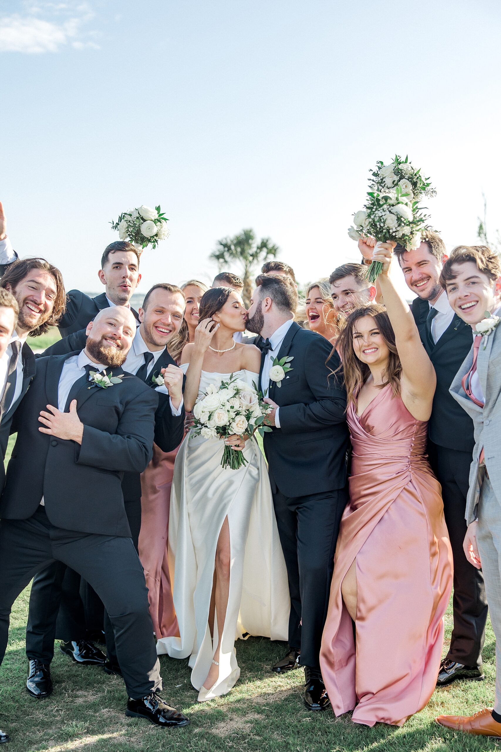 newlyweds kiss with wedding party surrounding them