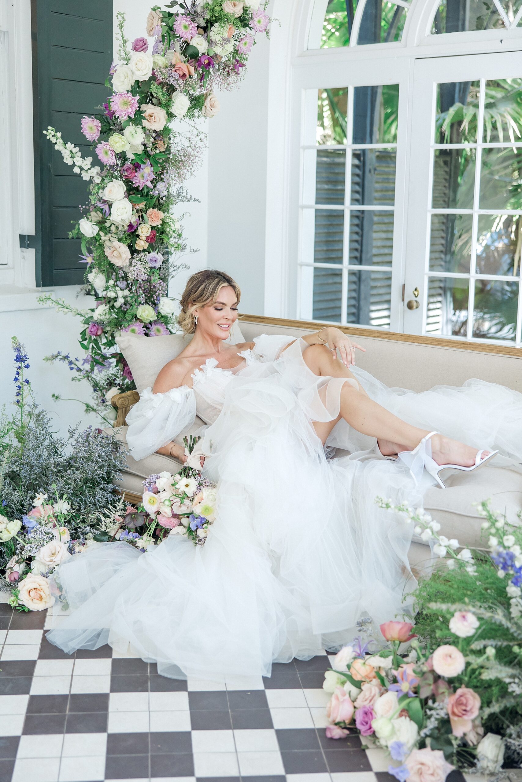 bride sits on couch surrounded by elegant spring florals