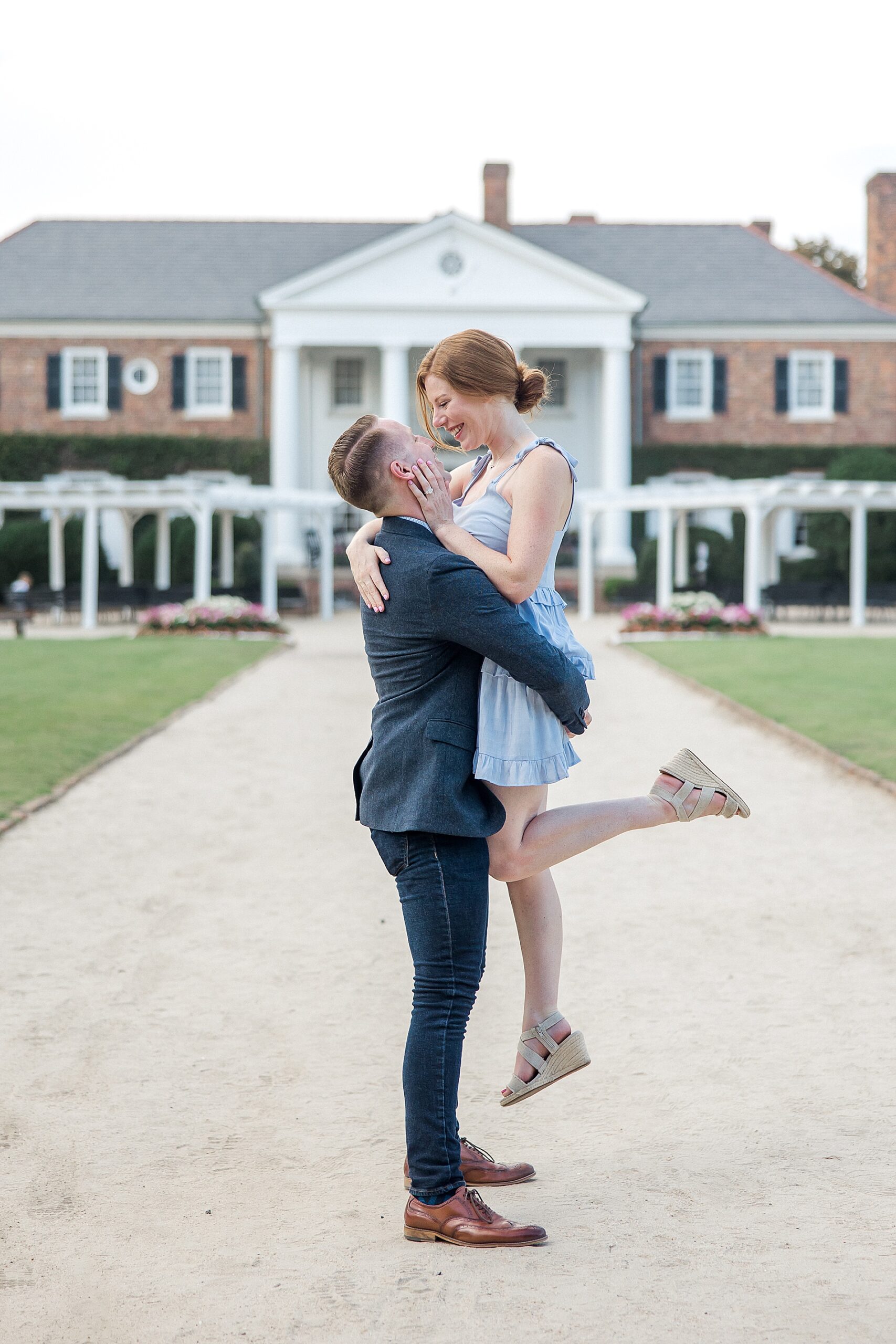 guy lifts his fiancé up in front of estate at Boone Hall