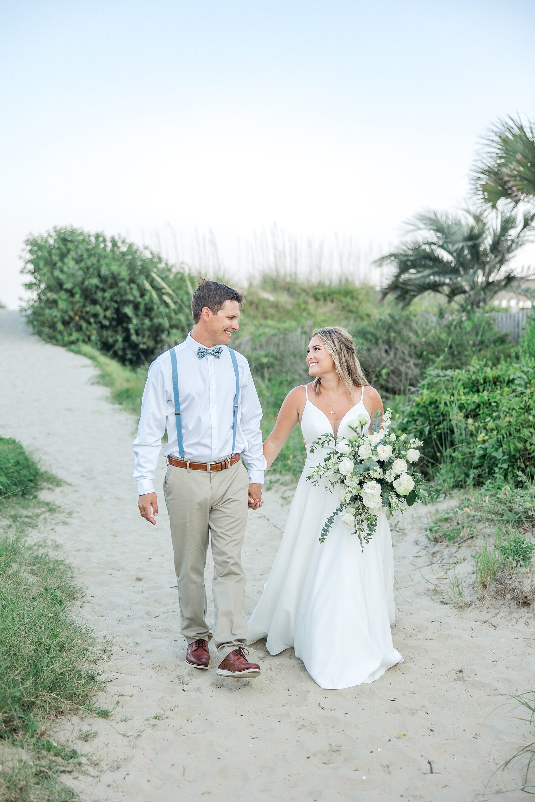 bride and groom hold hands and walk along the beach