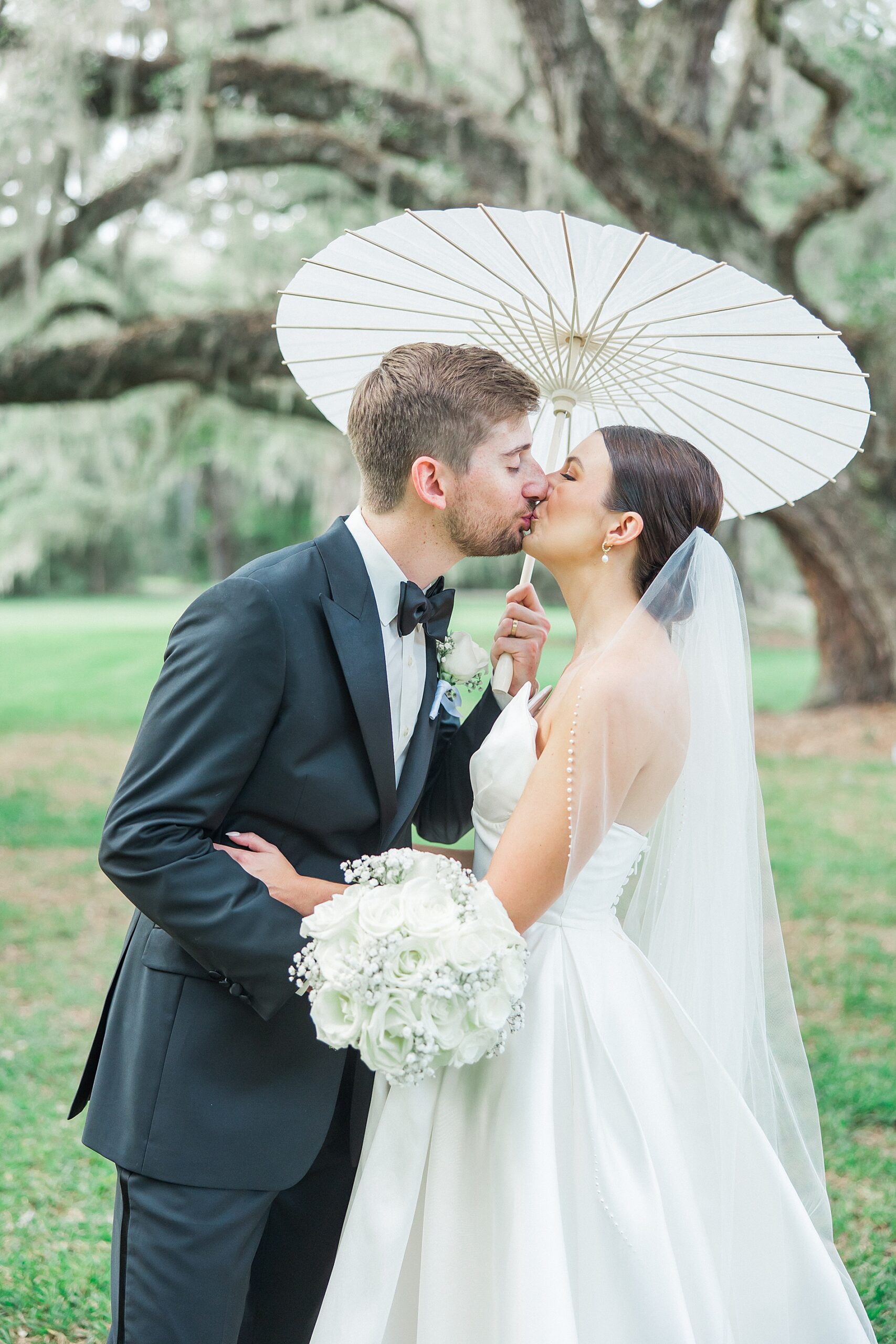 newlyweds kiss under parasol at Timeless Charleston Wedding  at Magnolia Plantation