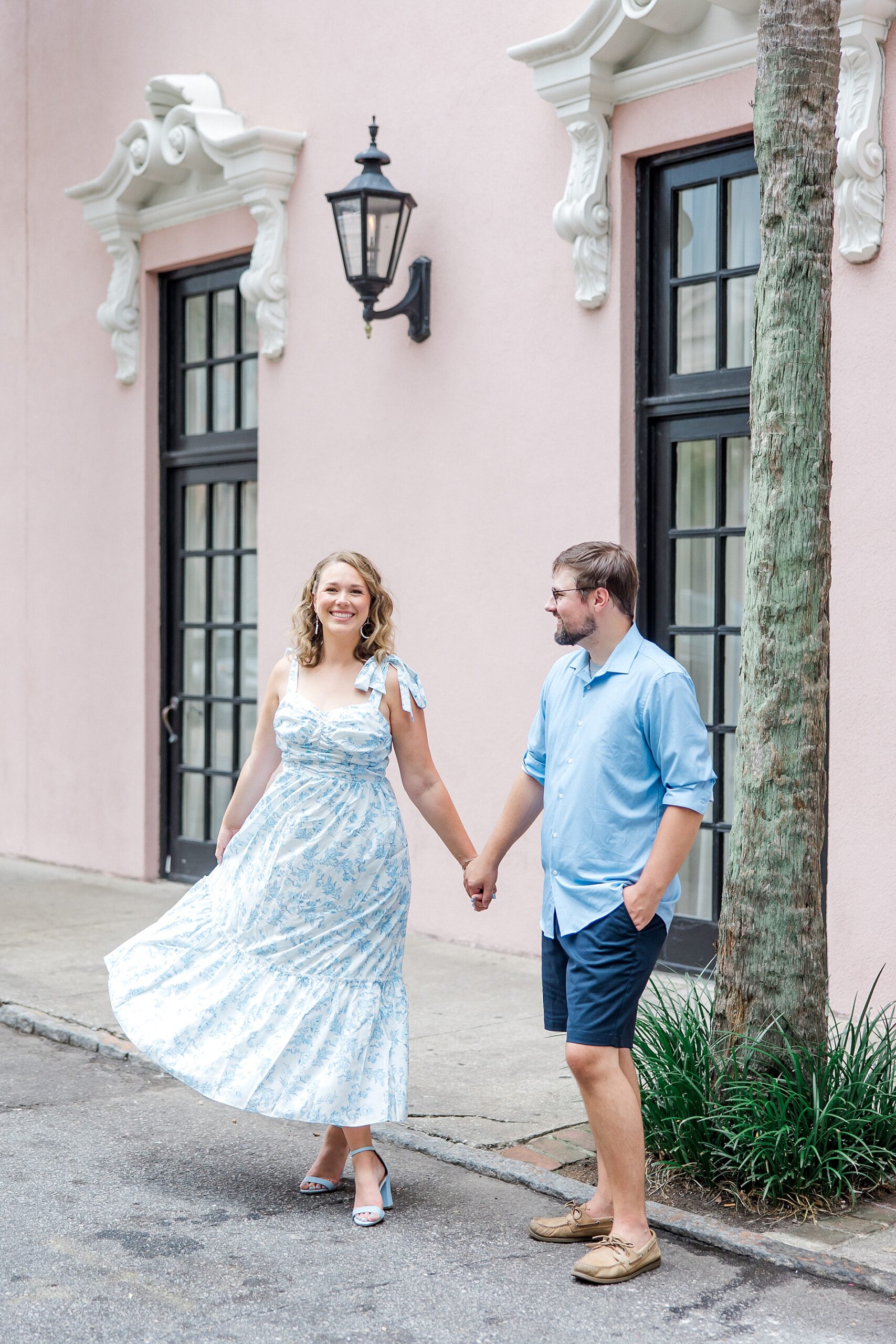 couple walk together holding hands by pink building in downtown Charleston