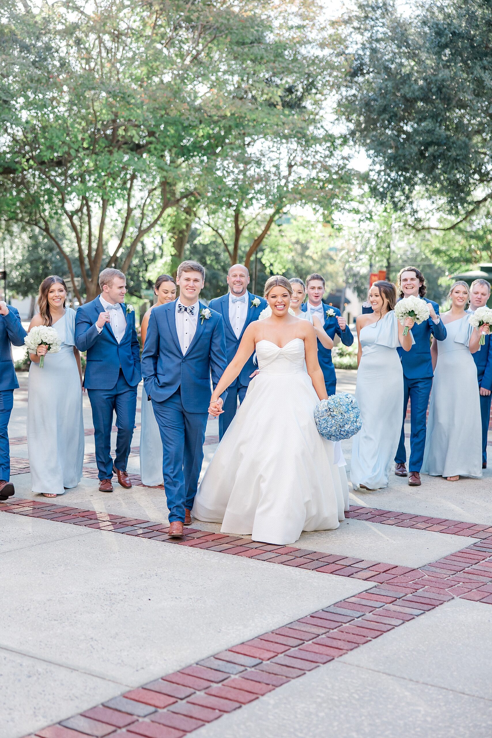 bride and groom walk together holding hands with wedding party walking behind them