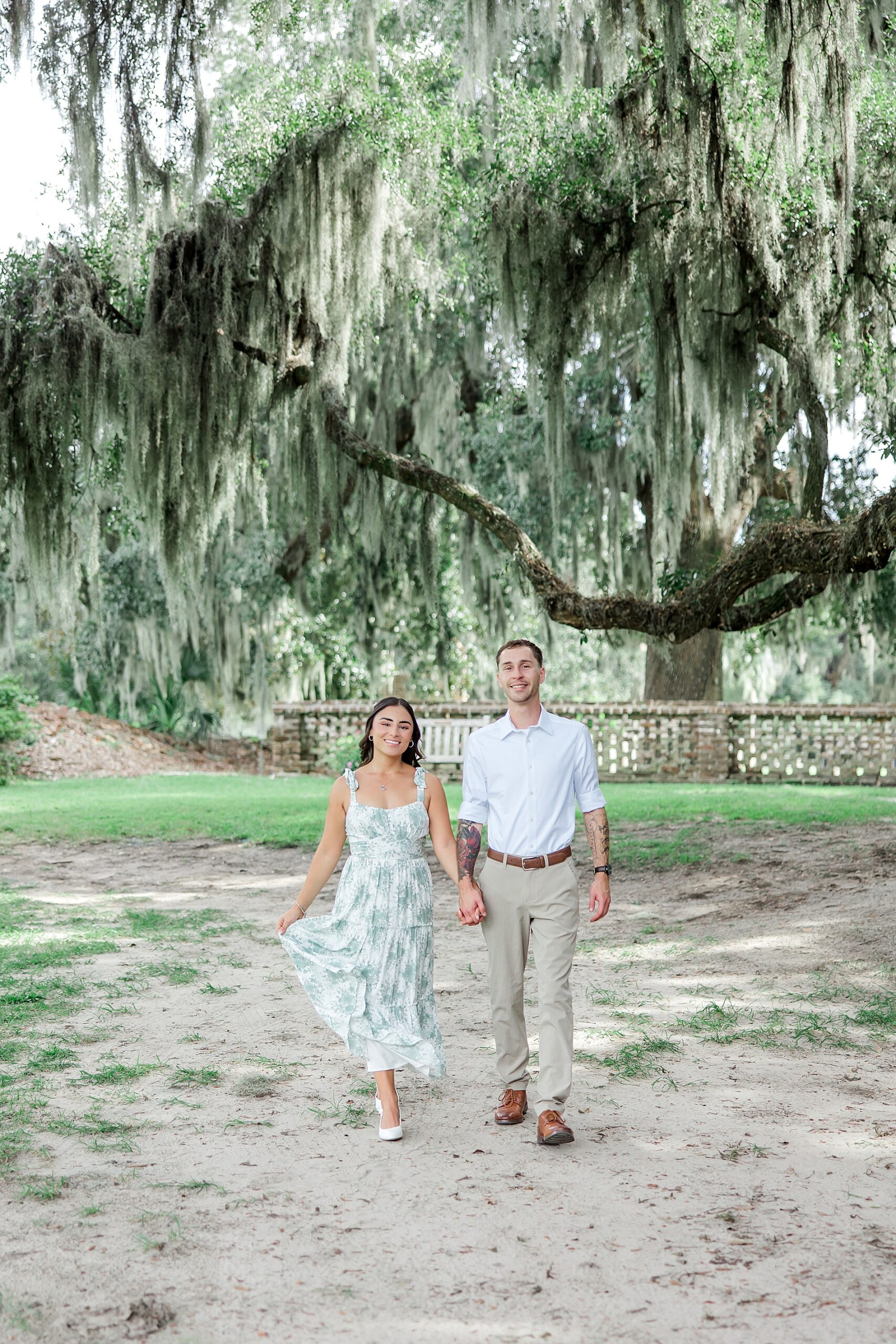 engaged couple walk through gardens with ancient oaks covered in Spanish moss